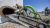 Two team members stand directly behind a robotic crawler with a green-tube arm, going up a ramp and entering a sulfur tank