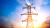 Power lines are held up by a tower with the sun setting in the background