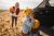 Photo of a cute little boy putting pumpkins into a car trunk, accompanied by his mother; going back home after spending his day on a lovely pumpkin patch and picking pumpkins; fall activities for families with young children.