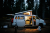 Toddler boy looking out side door of camper van parked in forest at night while father prepares camp